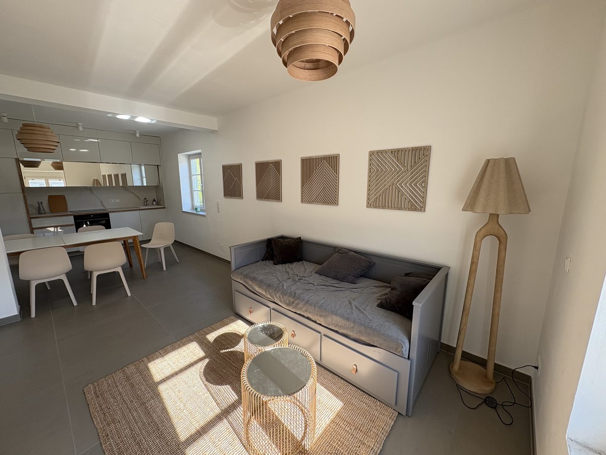 Helles, modernes Wohnzimmer mit Schlafsofa und offener Küche im Kaufhaus Wiedenig